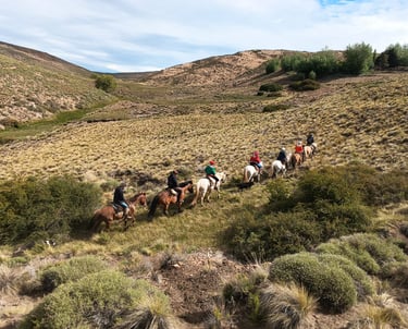 A group of people on horseback riding in a line through a hilly landscape.