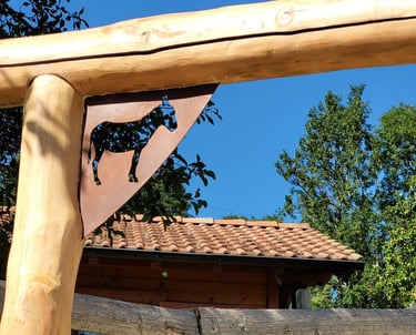 Rustic log fence post with a decorative donkey metal cutout on a farm under a blue sky.