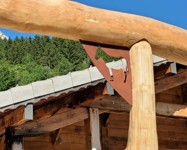 Rustic wooden alpine chalet featuring a decorative metal cow silhouette bracket against a clear blue sky.