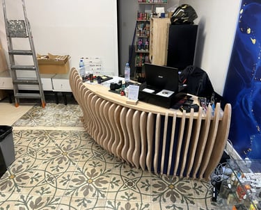 Modern curved wooden slat reception desk in a shop with patterned floor tiles and shelving.