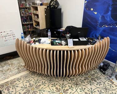 Modern curved wooden reception desk with vertical slats in a shop with patterned floor tiles.