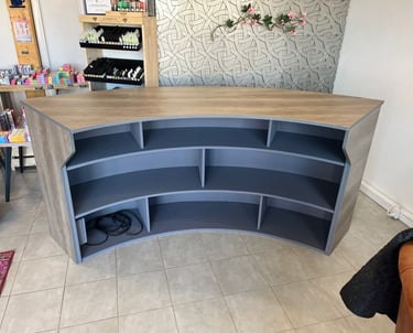 Curved wood and grey reception desk with open shelving for a retail store or boutique checkout.