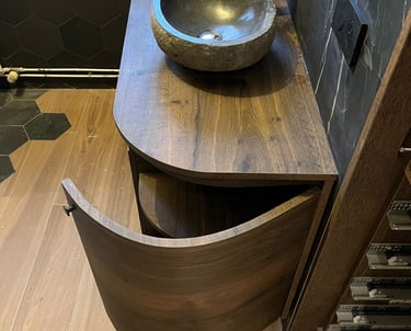Modern bathroom vanity with double stone vessel sinks and a curved dark wood cabinet.