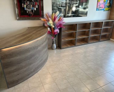 Modern curved wooden reception desk with matching shelving unit and colorful pampas grass decor.
