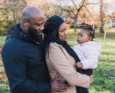 a man and woman holding a baby in a park in Bexley smiling towards the baby