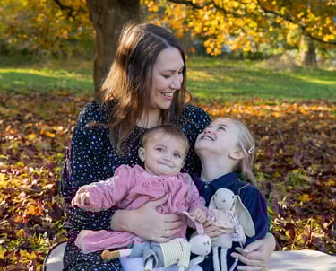 a woman sitting on a blanket with two children smiling towards the older girl who looks back smiling