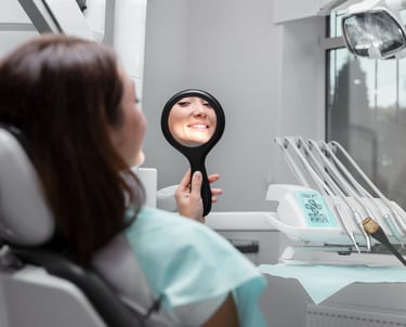 Una mujer sonriendo en un espejo en clinica dental, feliz de sus resultados
