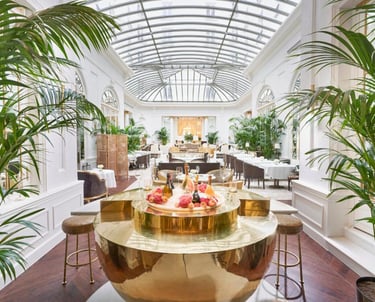 Palm Court Lounge – Elegant glass-roofed dining space with lush greenery and a golden champagne bar.