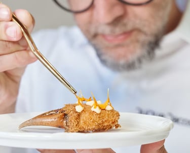 Chef Quique Dacosta garnishing crab claw with edible flowers using tweezers.