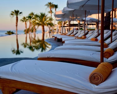Luxury poolside loungers with umbrellas overlooking palm trees and the ocean.