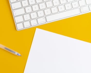 A White Keybord, Pen, and Sheet of Paper on Yellow Background