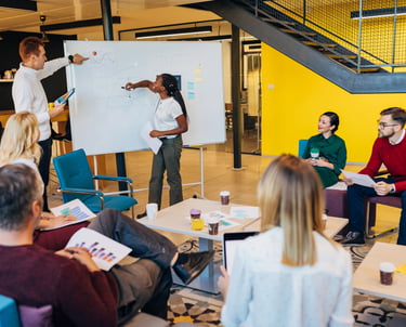 Female business coach giving presentation on whiteboard at team business training