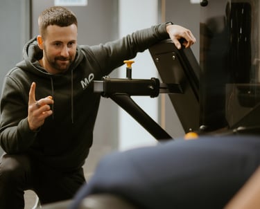 Personal trainer in hoodie coaching client on gym equipment in Leamington Spa fitness centre, focused on technique and su