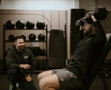 Trainer observing client’s seated dumbbell shoulder press in Leamington Spa gym, highlighting coaching and strength training.