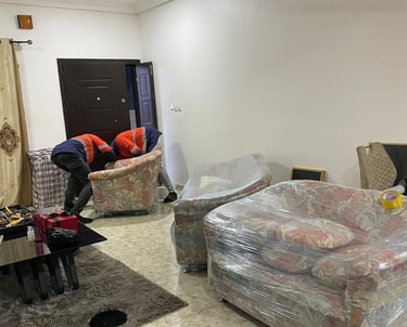 Two professional movers in orange high-visibility jackets with reflective strips collaborate to lift