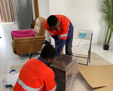 Two professional movers in orange high-visibility vests with reflective stripes collaborate to wrap 