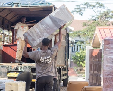 Two movers, one inside an open-back truck and another outside, lift large wrapped boxes and panels d