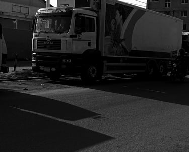 A black and white photograph of a white MAN refrigerated delivery truck with "BRAEM TRUCKS.COM" bran