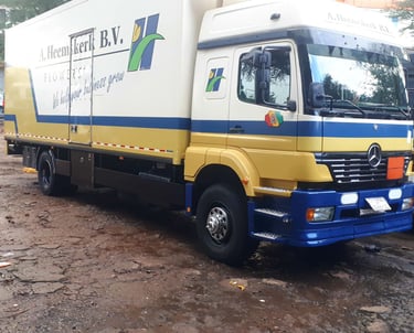 A yellow and blue Mercedes-Benz delivery truck branded "A. Heemskerk B.V." with green flower motifs
