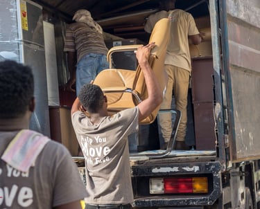 Three professional movers from TE Transporter Express team up to load a beige leather armchair into 