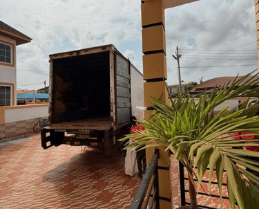 An open white moving truck with weathered sides and license plate visible, parked on a wavy red bric