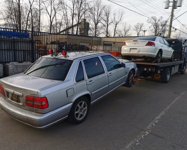 A scrap Volvo car being towed by a tow truck