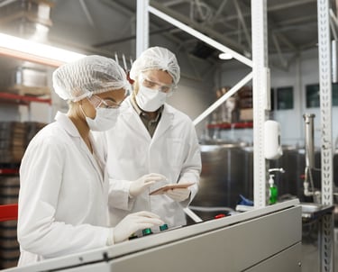 Two laboratory technicians wearing white coats and masks operating machinery in a food processing plant.