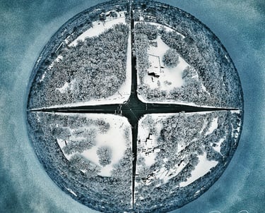 Tiny planet aerial view of a four-way street intersection surrounded by snow-covered trees and homes.