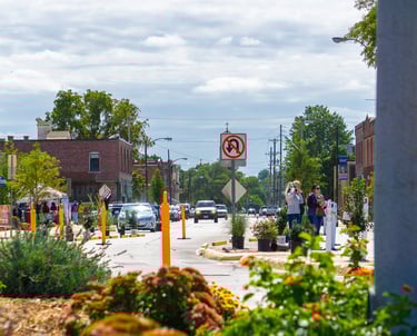 Urban street scene featuring temporary planters, traffic barriers, and pedestrians during a community event.