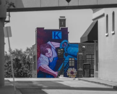 Urban mural of a labor figure on the Kansan Building, with selective color against a grayscale streetscape.