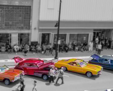 Colorful classic cars parked along a city street, with pedestrians and buildings shown in black and white.