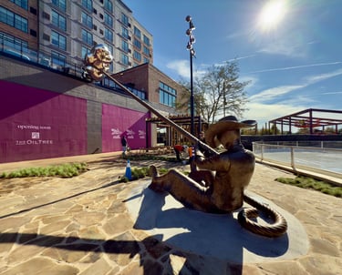 Bronze cowboy statue holding a long lasso rope in a modern outdoor urban courtyard with stone paving.