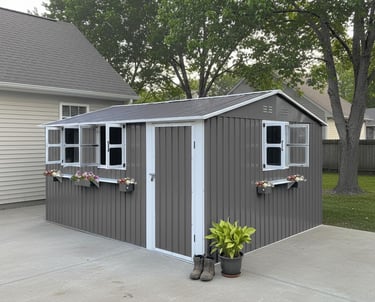 Modern grey metal garden storage shed with white trim, windows, and flower boxes on a concrete patio.