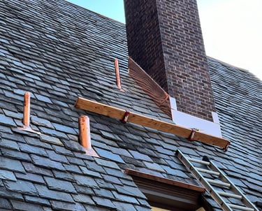 Professional roof repair featuring new copper flashing installed around a brick chimney and vent pipes.