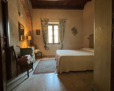Rustic Tuscan style bedroom featuring a dark wood beamed ceiling, stone archway, and cozy queen bed.