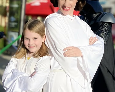 A young girl and woman in Princess Leia costumes pose with Darth Vader at a Star Wars event.