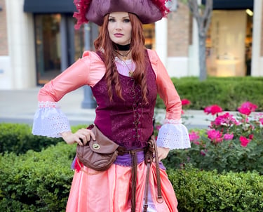 A woman in a detailed pirate costume with a feathered tricorn hat and corset standing in a garden.