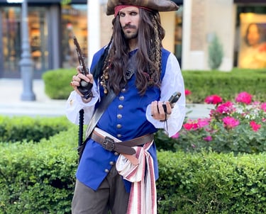 A man in a detailed Jack Sparrow pirate costume holding a flintlock pistol and compass in a garden.