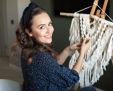 Mujer sonriendo mientras crea un tapiz de macramé hecho a mano con cordón de algodón blanco