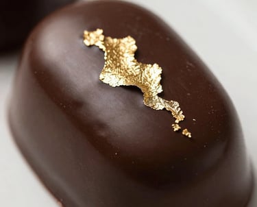 Gourmet photography of a glossy dark chocolate entremet with gold leaf decoration, mirror glaze finish, high-end culinary magazine style, Western European / French.