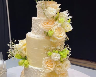 Elegant four-tier white wedding cake decorated with fresh peach roses and baby's breath.