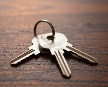 A macro photograph of high-end property keys resting on a solid dark wood table with soft copper lighting in the background.