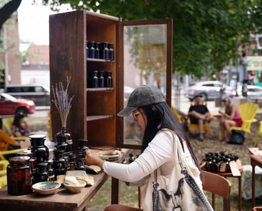 A woman wearing a baseball cap sits at a table in a park participating in an art installation