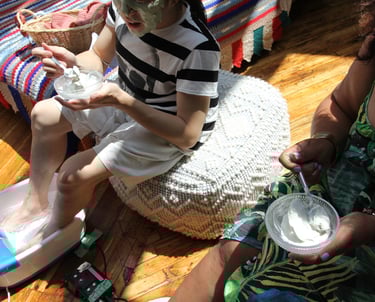 Two People eat ice cream while soaking their feet in bubbly foot baths while sitting on giant poofs.