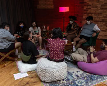 About 10 people sit on soft seats talking around a coffee table.
