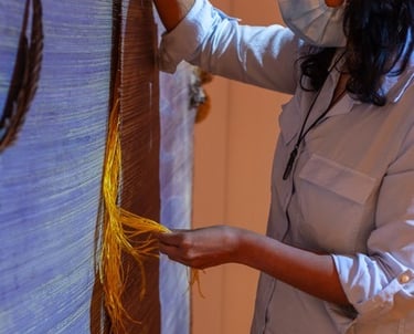 Masked woman with long black hair uses a tactile screen made of invasive grass and natural objects.