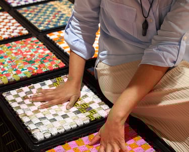 Woman on milk crates touching colorful Punjabi textiles arranged around her.