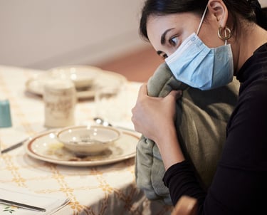 Une femme portant un masque tient un coussin vibrant rempli d'épices chai sur une table de cuisine