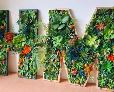 Decorative wall art spelling HM featuring vibrant artificial succulent arrangements in wooden letter frames.