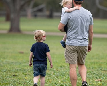 A father playing with his children in a sunny park, smiling and engaged.